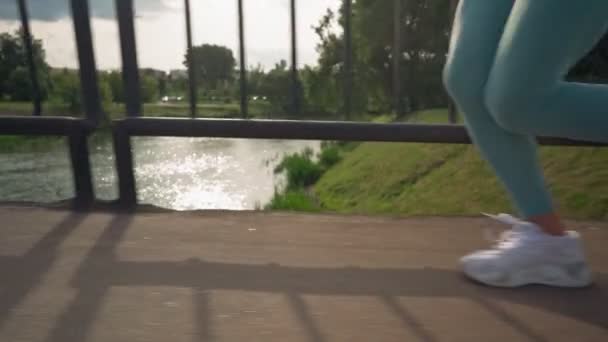 Vista de cerca de los pies femeninos corriendo por una carretera asfaltada hacia el atardecer — Vídeos de Stock