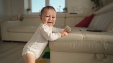 Sevimli bebek kanepeye yaslanmış ayağa kalkmayı öğreniyor. Sevimli çocuk kanepeye tutunmayı öğreniyor.