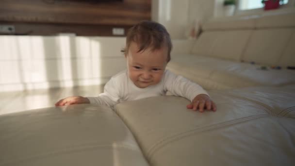 Lindo bebé niño que se apoya en el sofá aprendiendo a ponerse de pie. Adorable niño aprendiendo a estar de pie sosteniéndose en el sofá — Vídeo de stock