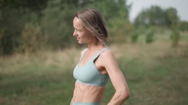 Güneşli bir günde ormanda koşan sarışın, beyaz bir kadının orta boy paralel pozu. Tepedeki kadın koşucu durağı. Odaklanmış sporcu kız gökyüzüne bak