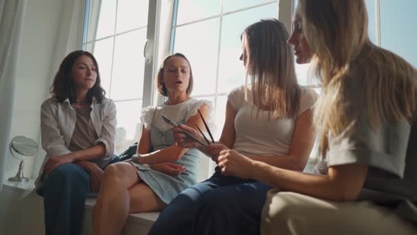 Chicas divirtiéndose en alféizar ventana. Cuatro chicas caucásicas sentadas en el alféizar de la ventana discuten algo y lough. Escuela de arte taller. — Vídeos de Stock