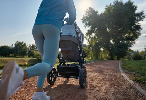 Aktif anne koşusu. Sabahları bebek arabasıyla yürüyen bir kadın ya da koşu. Anne bebek arabasında koşuyor..