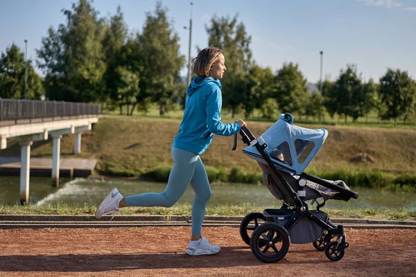 Active mother jogging. Jogging or power walking woman with a baby stroller in morning. Mother with child in stroller running.