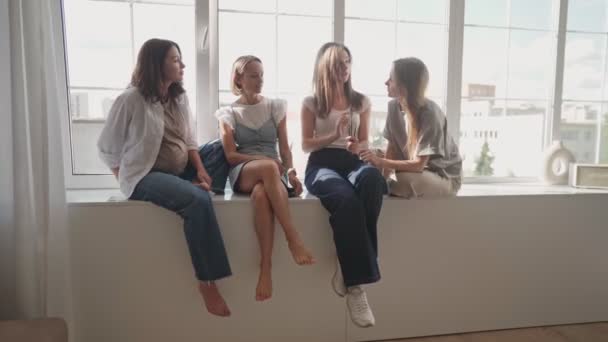 Girls having fun on window sill. Four caucasian girls sitting on window sill discuss something and lough. Art school workshop. — Stock Video