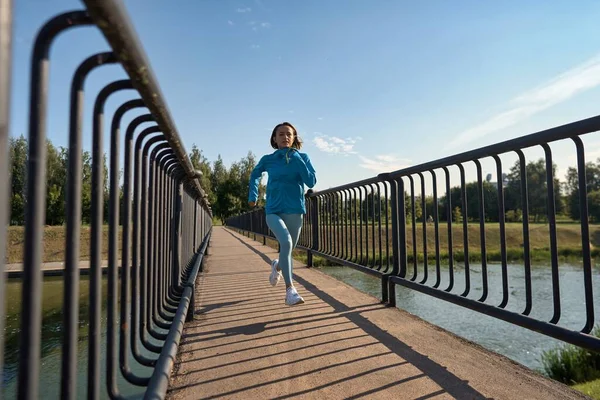 Mooie vrouwelijke jogger loopt in de ochtend over brug. — Stockfoto