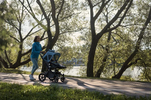 Active mother jogging. Jogging or power walking woman with a baby stroller in morning. Mother with child in stroller running.