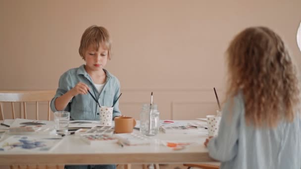 Groep kinderen en hun leraar leunend over tafel met aquarelverf en het schilderen van zelfgemaakte klei items. Kinderen met leraar in de kunstklas — Stockvideo