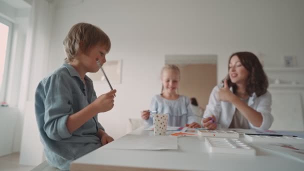 Grupp av barn och deras lärare lutar sig över bordet med akvarell färger och måla egengjorda lera objekt. Barn med lärare i konstklass — Stockvideo
