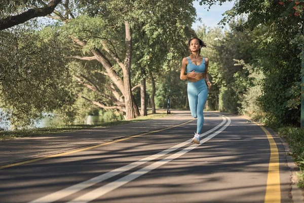 Jonge atletische vrouw joggen op de weg in de ochtend — Stockfoto