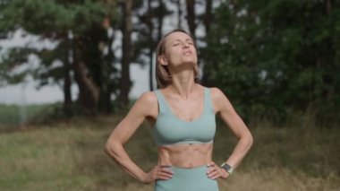 Güneşli bir günde ormanda koşan sarışın, beyaz bir kadının orta boy paralel pozu. Tepedeki kadın koşucu durağı. Odaklanmış sporcu kız gökyüzüne bak