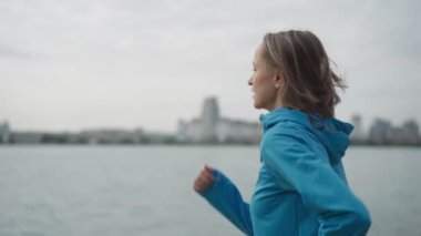 Nehir kenarındaki bir parkta spor giyim kuşamında ağır çekimde çalışan genç bir bayan. Spor salonundaki kadın dışarıda koşuyor. Sağlıklı aktif yaşam biçimi