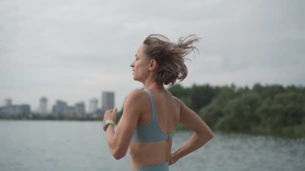 Ralentissez Jeune sportive en tenue de sport dans un parc près de la rivière. Fitness femme jogging extérieur. Mode de vie sain et actif — Video
