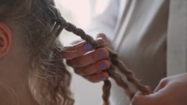 Sarışın, kıvırcık saçlı güzel bir kız aynada aynadaki yansımasına bakarken annesi at kuyruğu yapıyor.