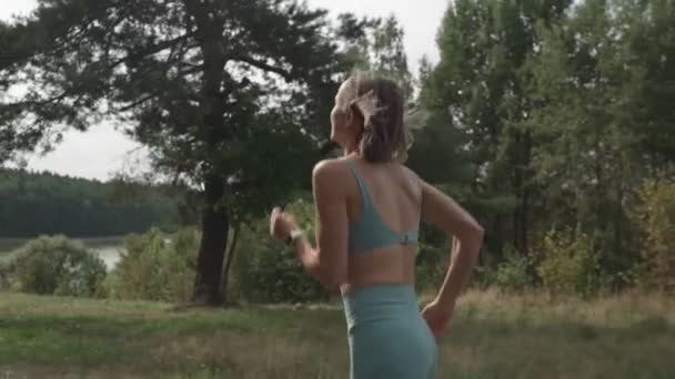Vista lateral de uma mulher correndo colina acima em uma floresta. — Vídeo de Stock