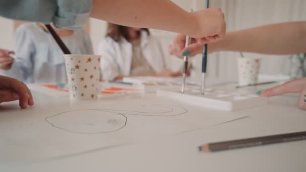 Eine Gruppe Kinder und ihre Lehrerin lehnen sich mit Aquarellfarben über den Tisch und bemalen selbstgemachte Gegenstände aus Ton. Kinder mit Lehrer im Kunstunterricht — Stockvideo