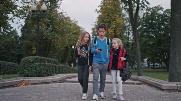 Μέτριο πλάνο τριών μαθητών με σακίδια να φεύγουν από το σχολείο και να μιλάνε. Αγόρι και δύο κορίτσια επιστρέφουν από το σχολείο. — Αρχείο Βίντεο