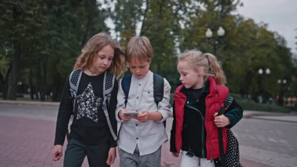 Medium shot van drie leerlingen met rugzakken die van school gaan en praten. Jongen en twee meisjes komen terug van school — Stockvideo
