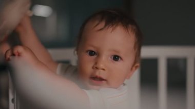 Genç anne ve bebek gece beşiğinde. Kadın çocuğa doğru eğildi, çocuk el kaldırdı.