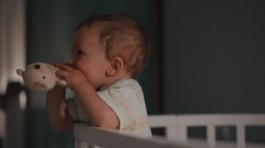 Genç anne ve bebek gece beşiğinde. Kadın çocuğa doğru eğildi, çocuk el kaldırdı.