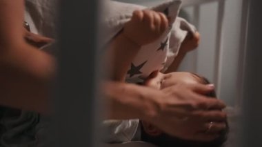 Sevimli yeni doğmuş erkek bebek, geceleri beşikte uyumak istemiyorum. Anne bebeği yatırır.