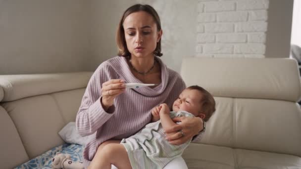 Mãe medir a temperatura de seu filho doente no fundo. Criança doente com febre alta deitada no sofá em casa . — Vídeo de Stock