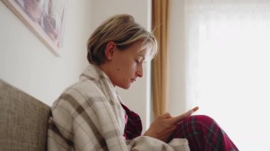 Adet döngüsü takvimini akıllı telefonunda takip uygulaması ile kontrol eden bir kadının yakın çekimi. Rahat bir pozisyonda oturan rahat kırmızı pijama giyiyor. Regl sağlık ve benlik kavramı