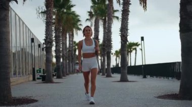 Genç Avrupalı bir kadın sabahın erken saatlerinde elinde spor minderiyle güneşli bir parkta yürüyor. Aktif giysi giyiyor ve odaklanmış ve enerjik görünüyor. Sağlıklı yaşam tarzı ve sabah rutini kavramı