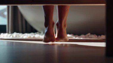 Sabahları güneşli bir yatak odasında, tahta zeminde çıplak ayakla yürüyen genç bir kadının yakın çekimi. Yavaş yaşam, farkındalık ve günün barışçıl başlangıcı kavramı. Yüksek kalite 4k görüntü