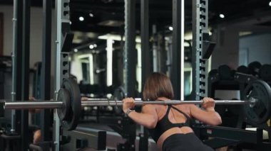 Atletik kadın modern bir spor salonunda halter çömelmesi yapıyor. Bacak ve kalça kasları için güç eğitimi, odaklanmış egzersiz, güç ve dayanıklılık. Fitness yaşam tarzı, sağlıklı vücut, halter egzersizi..