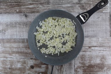 pan with frying  onion   on wooden table,close up