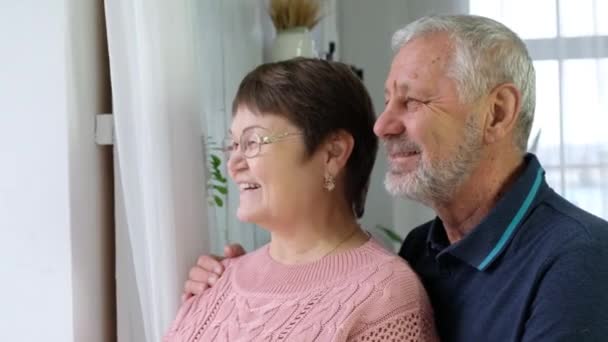 Vrolijke senioren familie koppel knuffelen lachen kijken naar raam, glimlachen — Stockvideo