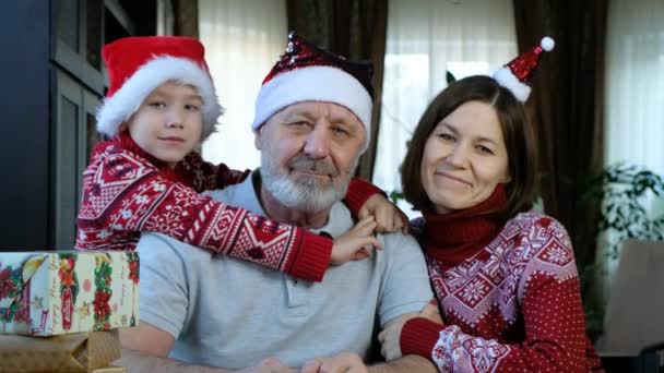 Feliz hombre mayor con barba en sombrero de Navidad rojo con su nieto y su hija adulta, celebrando el año nuevo — Vídeo de stock