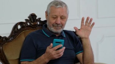 Senoir ayılı adam akıllı telefonla konuşuyor, web kamerasına bakıyor.