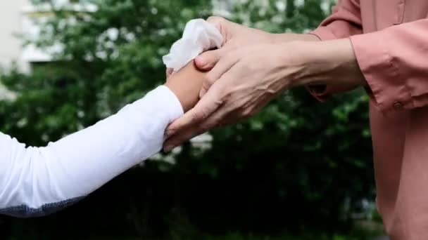 Женщина чистит детские руки влажной антисептической салфеткой, чтобы защитить от вируса короны и бактерий — стоковое видео