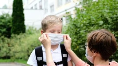 Anne ya da öğretmen okul çocuğuna tıbbi maske takıyor. Okula geri dönmek için karantina