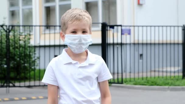 Маленький хлопчик залишається в школі і знімає медичну маску. Назад до школи . — стокове відео