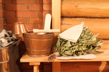 Bakır sauna aksesuarları ve meşe süpürgesi buhar odasındaki kaloriferin yanındaki tuğla duvarın arkasındaki bankta..