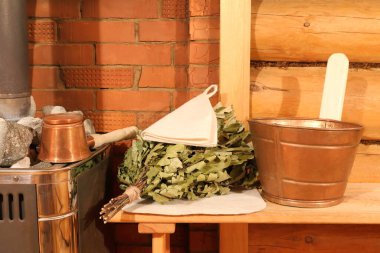 Bakır sauna aksesuarları ve meşe süpürgesi buhar odasındaki kaloriferin yanındaki tuğla duvarın arkasındaki bankta..