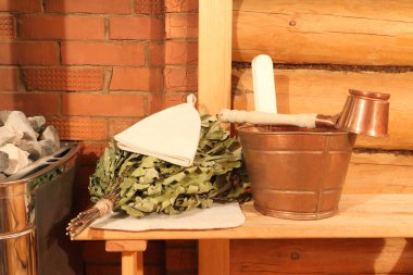Bakır sauna aksesuarları ve meşe süpürgesi buhar odasındaki kaloriferin yanındaki tuğla duvarın arkasındaki bankta..