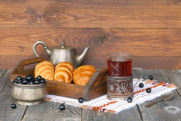 一只玻璃杯红茶 放在一盘羊角面包和一碗新鲜浆果旁边的木制底座上 — 图库照片