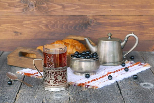 クロワッサンのトレイの近くの紅茶のガラスマグカップと木の背景に新鮮な果実のボウル — ストック写真