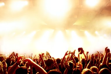 Parlak sahne ışıkları önünde konser kalabalığının siluetleri