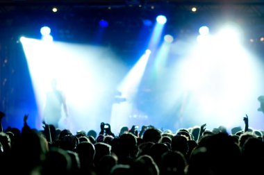 Parlak sahne ışıkları önünde konser kalabalığının siluetleri
