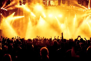 Parlak sahne ışıkları önünde konser kalabalığının siluetleri