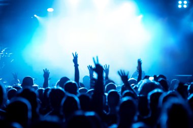 Parlak sahne ışıkları önünde konser kalabalığının siluetleri