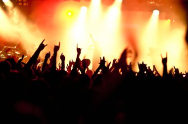 Parlak sahne ışıkları önünde konser kalabalığının siluetleri
