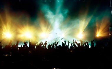 Parlak sahne ışıkları önünde konser kalabalığının siluetleri