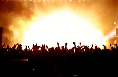 Parlak sahne ışıkları önünde konser kalabalığının siluetleri