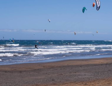 Tenerife 'deki El Medano plajında okyanus dalgaları üzerinde süzülen renkli uçurtmalarla spor meraklıları. Sörf ve aktif yaşam tarzı için mükemmel bir yer..