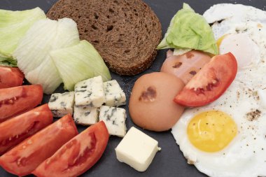 Koyu arkaplanda kızarmış yumurta, sosis, mavi peynir, marul ve domatesle kahvaltı. Sağlıklı yaşam tarzı ve yemek fotoğrafçılığı için lezzetli yüksek protein tabağı..
